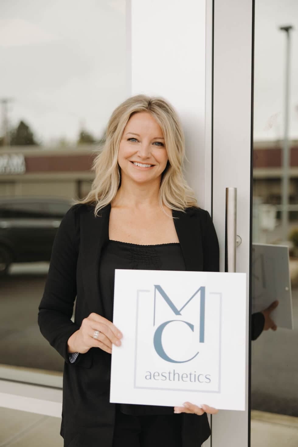 Melissa Cook, Founder of MC Aesthetics in McMinnville, in a Full-Body Portrait Holding a Sign, Highlighting Her Expertise in Aesthetic Treatments